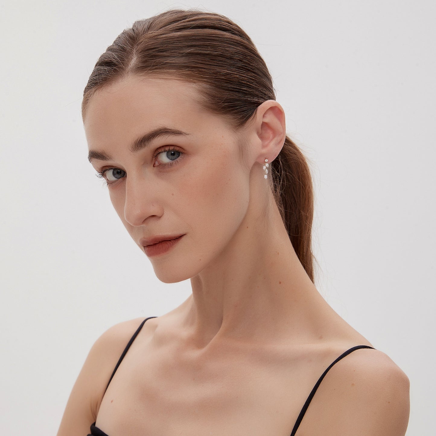 Woman with a ponytail wearing a black top against a white background