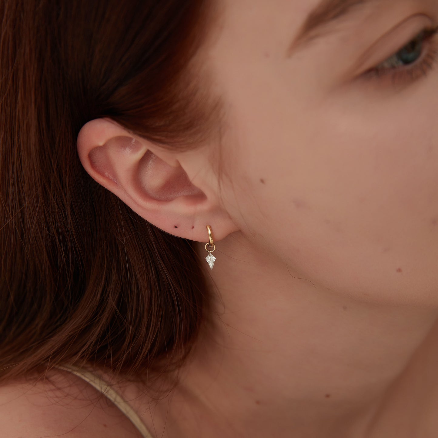 Close-up of a person wearing a gold earring with a small gemstone.