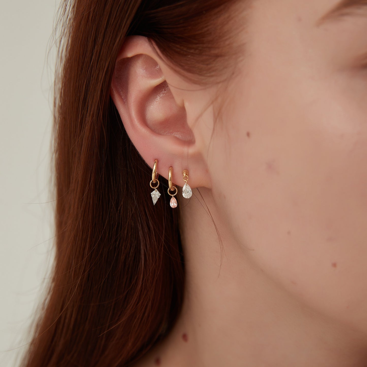 Close-up of a person wearing multiple earrings with a neutral background