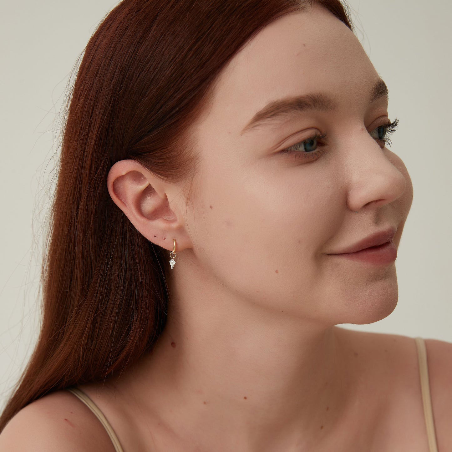 Woman with long brown hair wearing a beige top against a neutral background