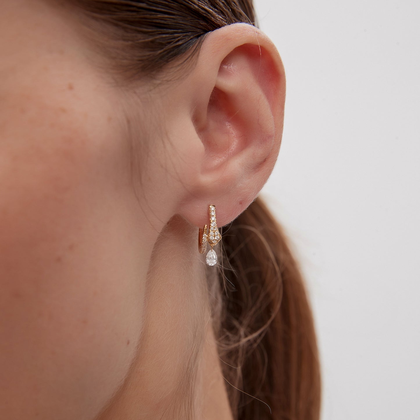 Close-up of a person wearing a pearl earring with a plain background
