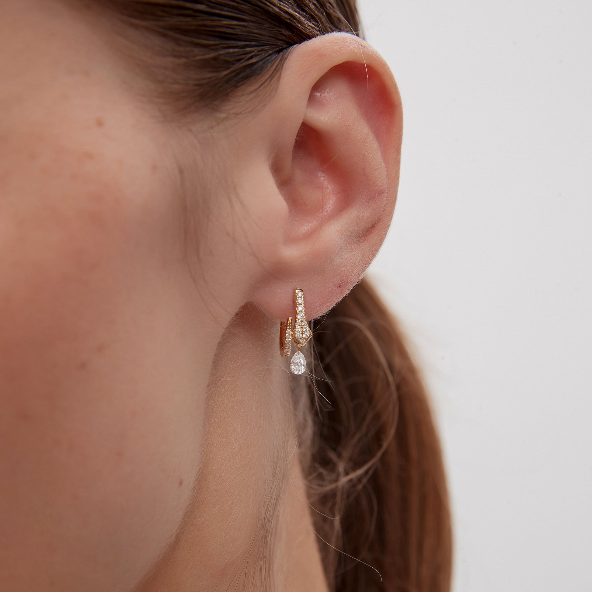 Close-up of a person wearing a pearl earring with a plain background