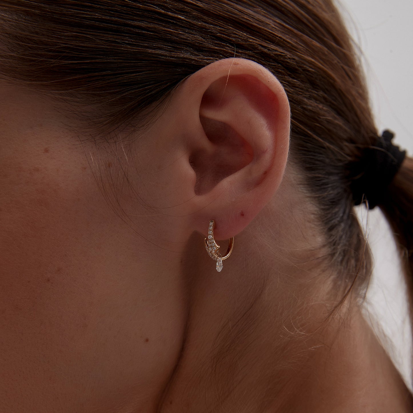 Close-up of a person wearing a gold hoop earring against a neutral background
