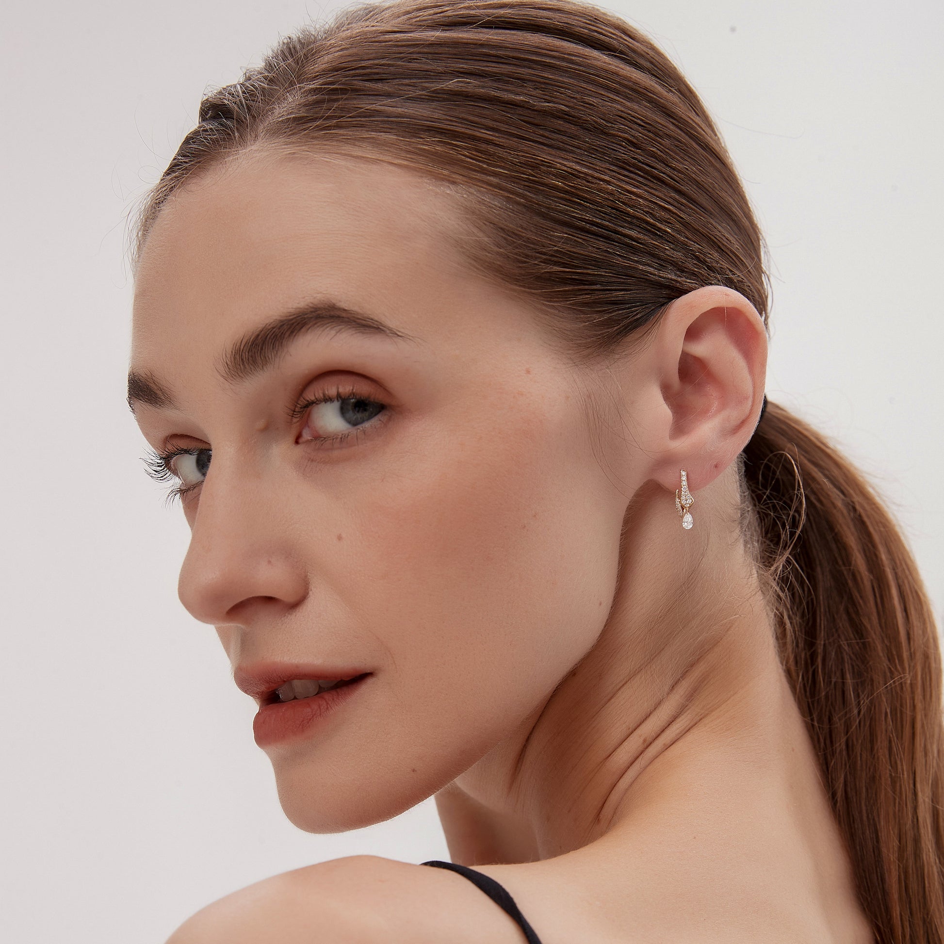 Woman with a ponytail wearing earrings against a plain background