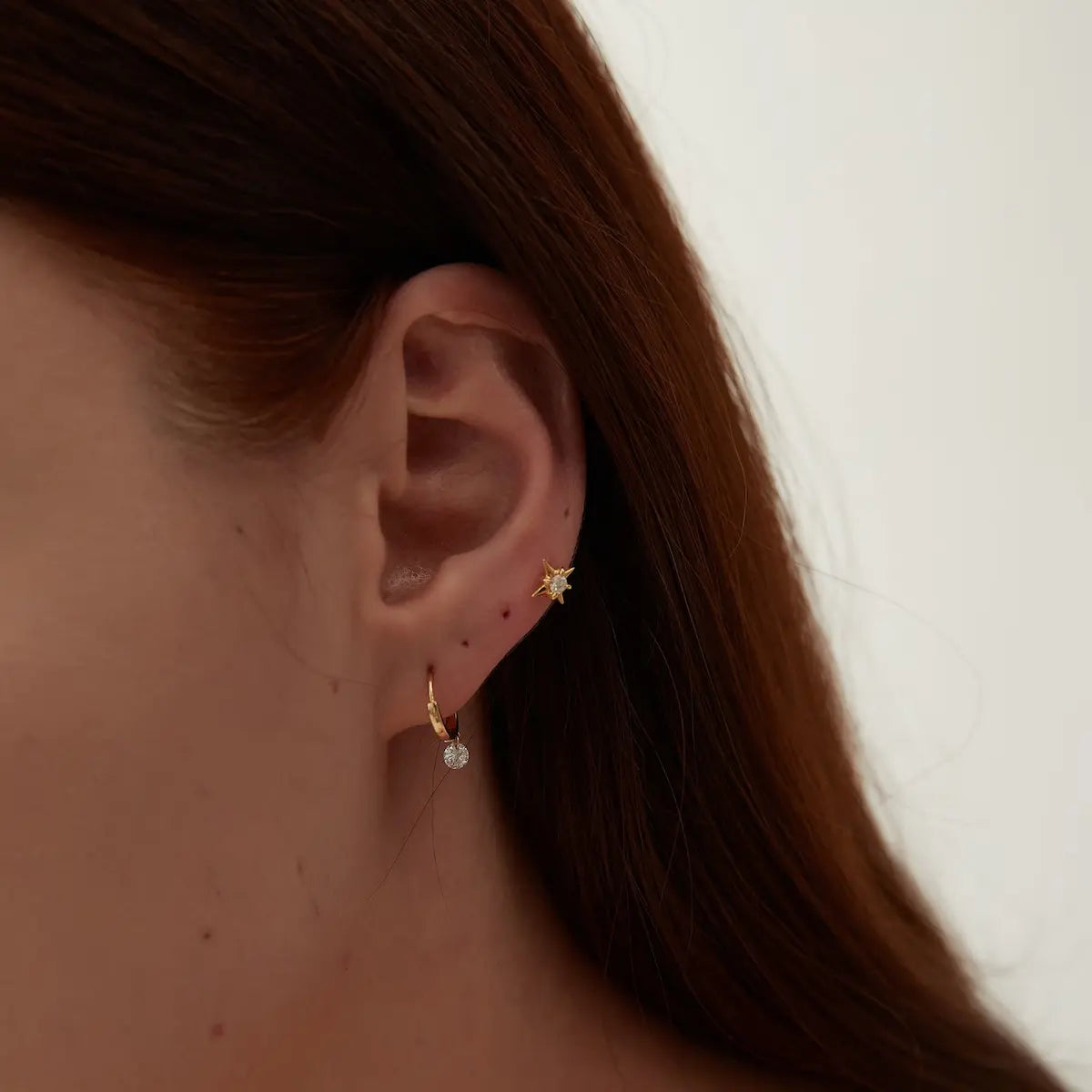 Model wearing the Round Diamond Dangle Hoop from the Radiant Drift collection. The suspended floating round diamond and sculptural gold hoop create cinematic brilliance, graceful movement, and modern editorial luxury jewelry styling.