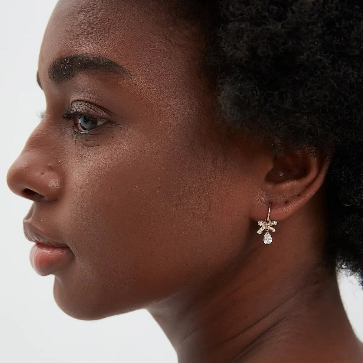 A professional lifestyle photograph showing the Butterfly Bow Pear Charm styled on an 18K solid gold hoop. The image demonstrates how the pear diamond drop captures light with every movement, adding a weightless sparkle to a curated ear stack. This perspective highlights the modular design and the narrative grace of the 'Celestial Drift' philosophy in a real-world setting. Captured in natural lighting to emphasize the fire of the D-E color diamond.