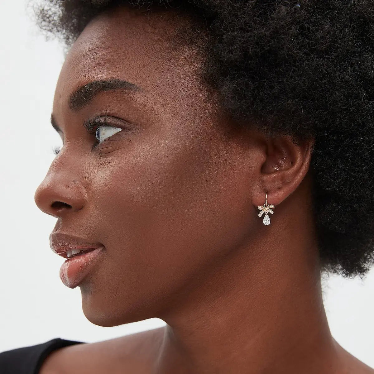 A technical side profile view of the Butterfly Bow Pear Diamond Charm. This image highlights the structural integrity of the 18K solid gold AU750 jump ring and the secure attachment of the bow and diamond drop. The side perspective showcases the slim and elegant profile of the charm, ensuring it sits perfectly on any hoop or stud for 24/7 wear. The consistent high-polish finish and the alignment of the brilliant pear diamond are clearly visible, emphasizing quality.