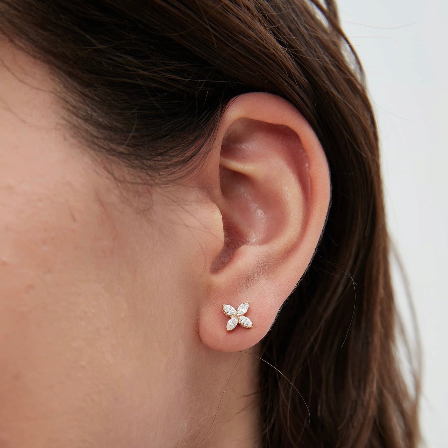 Close-up of a woman’s ear wearing a single clover diamond stud earring in 18K white gold, showing how the earring sits on the ear.