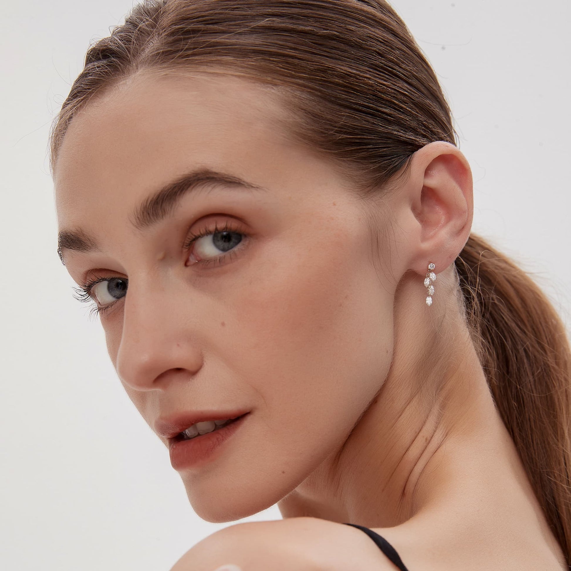 A lifestyle model shot of a woman wearing the Architectural Rhythm collection Round Stud Marquise Cluster Dangle in 18K solid gold. The photograph captures the natural movement and brilliance of the 0.50ctw white lab-grown diamonds as they catch light, offering a refined yet striking statement for a high-fashion look. This luxury jewelry piece by LTM Jewels embodies the blend of modern geometry and cascading light, making it an ideal gift for anniversaries or special occasions for a sophisticated woman.