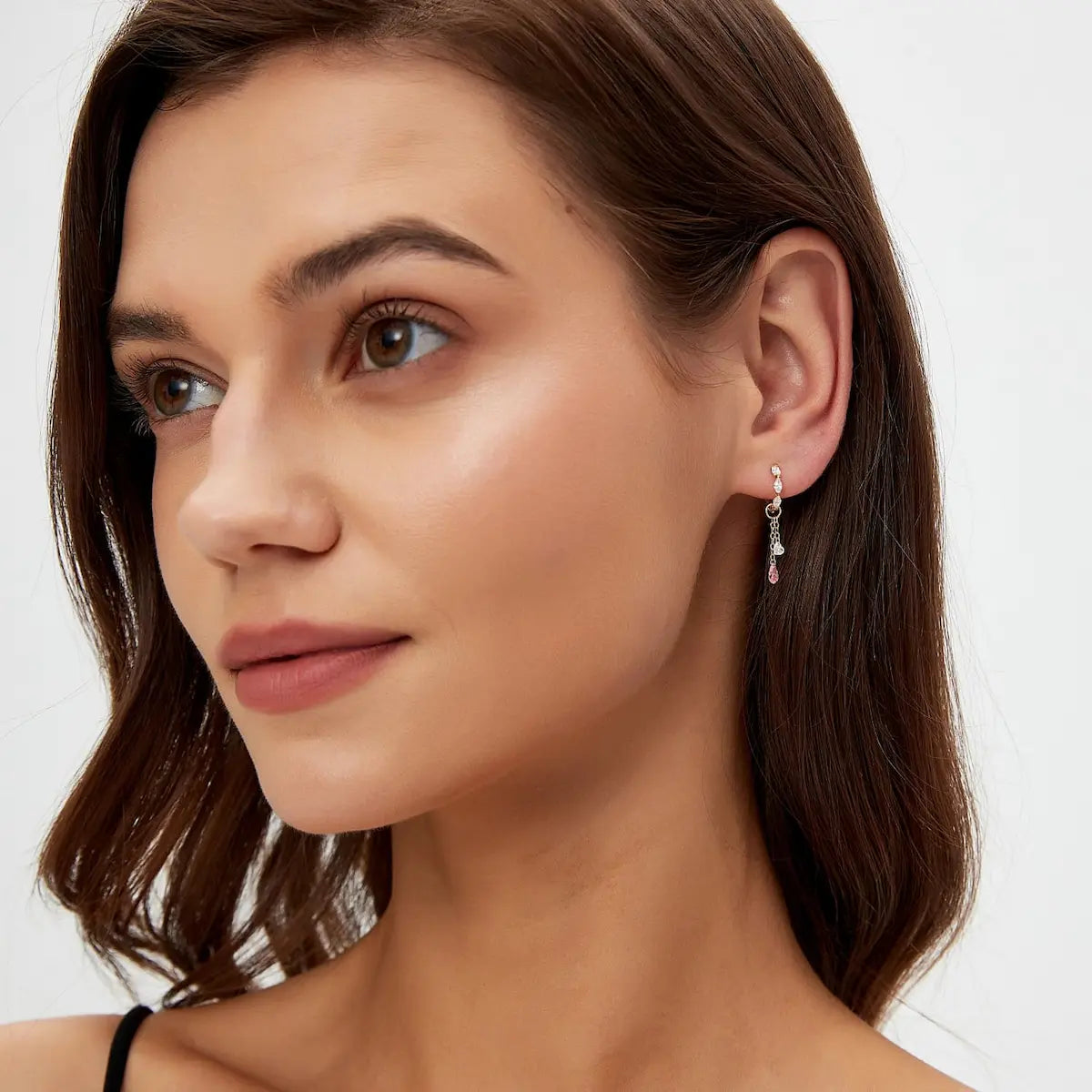 A fashion editorial image featuring a model wearing the Pink Pear White Heart Charm as part of a high-fashion ear curation. The photograph captures the poetic fusion of modern romance and architectural light, showcasing the charm's 0.30ctw diamonds against a cinematic aesthetic. The movement of the pear-cut dangle is frozen in time, illustrating its role as a contemporary heirloom designed to capture cherished memories with a vibrant, rhythmic dance of rare color.
