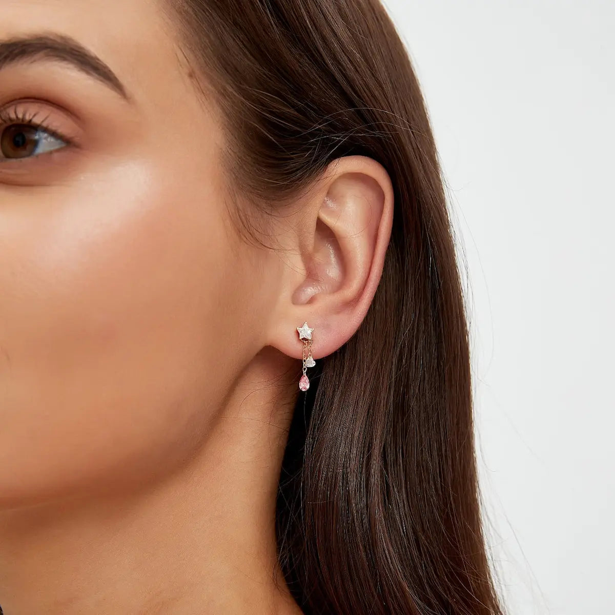 A professional lifestyle photograph showing the Pink Pear White Heart Charm styled on an 18K solid gold hoop. The charm demonstrates its kinetic motion, swaying gracefully to catch natural light. This perspective highlights the romantic color contrast between the pink and white diamonds and how the laser-drilled stones appear to float within a sophisticated, curated ear stack. The high-polish gold and brilliant diamond fire create a cinematic radiance for luxury daily wear.