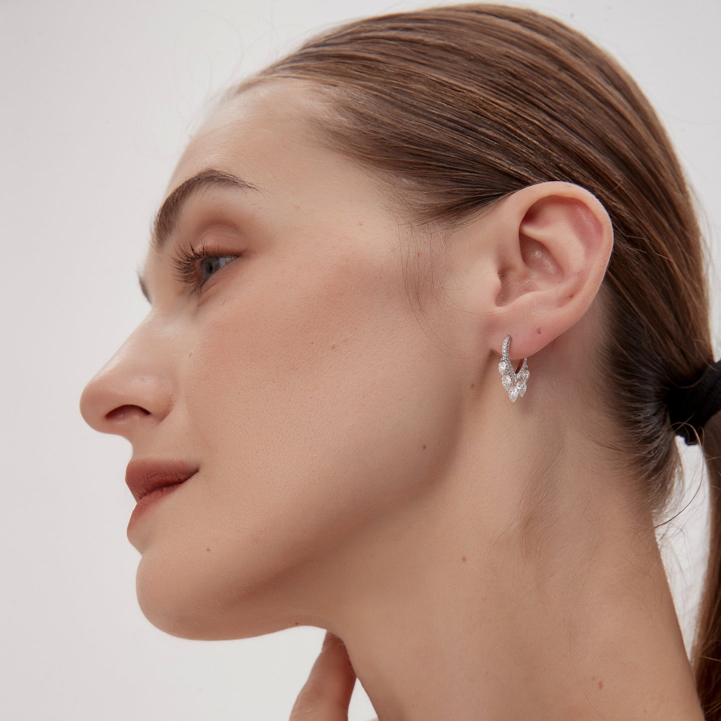 Close-up of a woman wearing a silver earring against a plain background