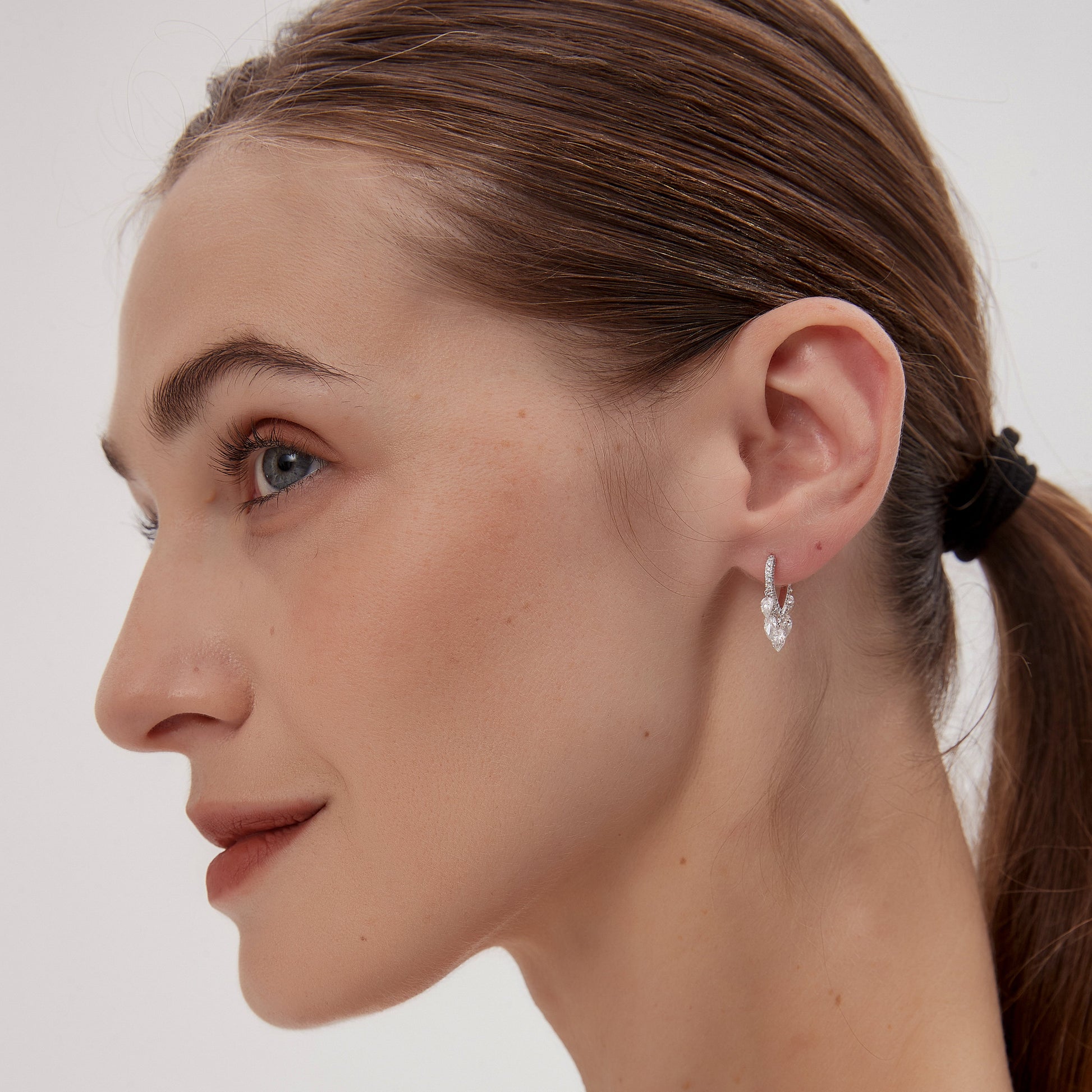 Close-up of a woman wearing a silver earring against a plain background