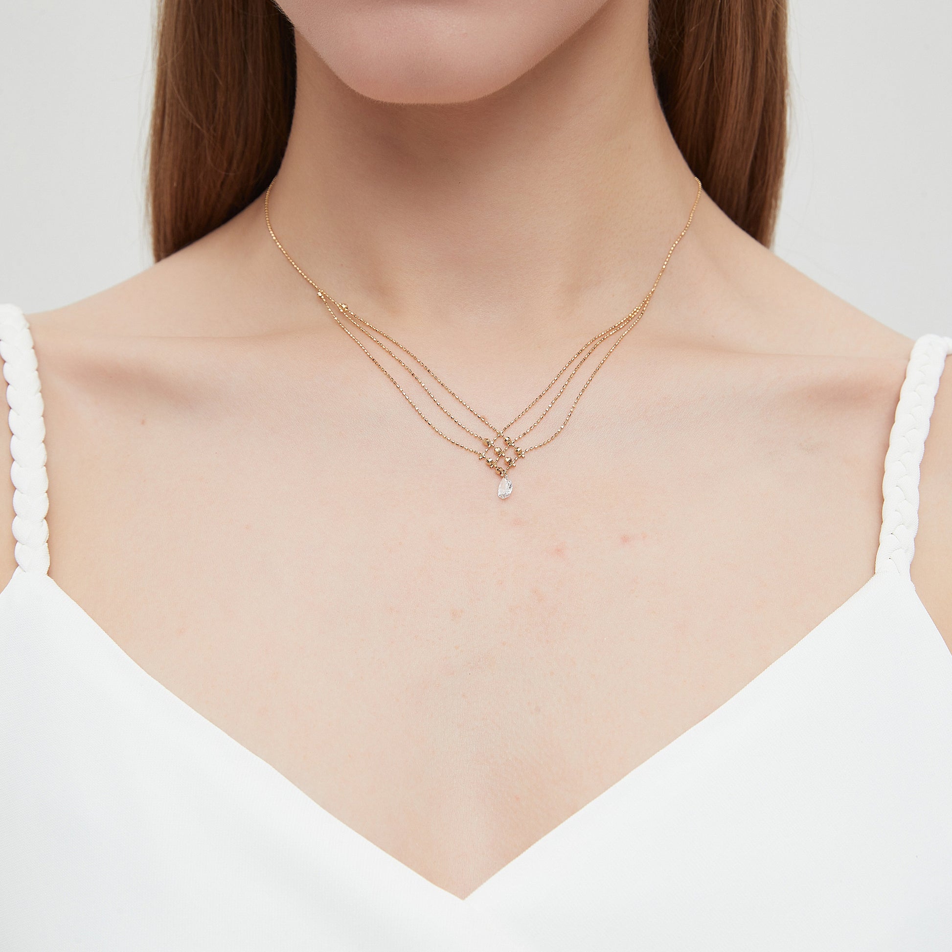 Woman wearing a delicate gold necklace with a plain background