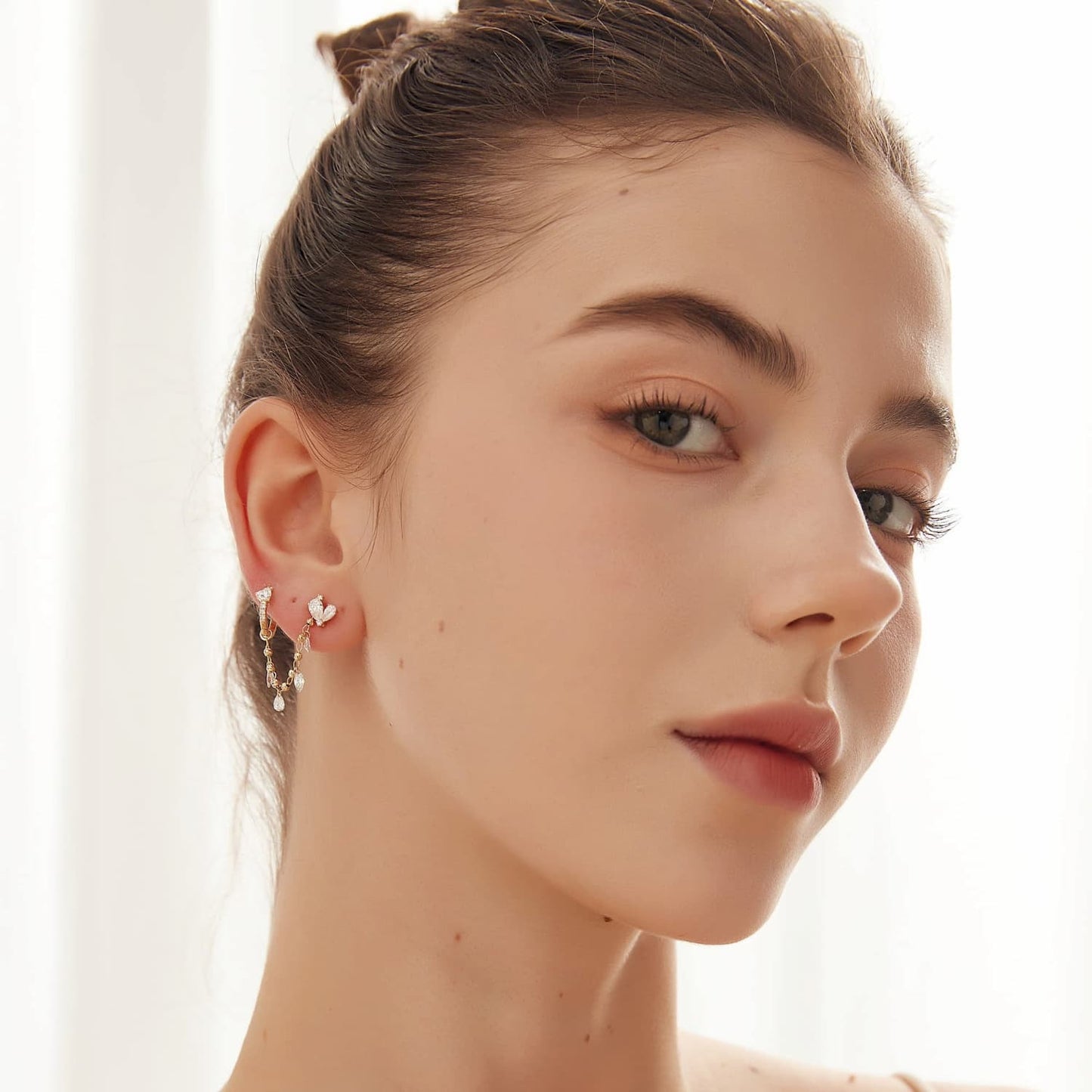 A fashion editorial shot of a model wearing the Gilded Bead & Diamond Dangle Charm. Illustrates the piece as a modern essential for a luxury curated ear stack, capturing light with every movement.