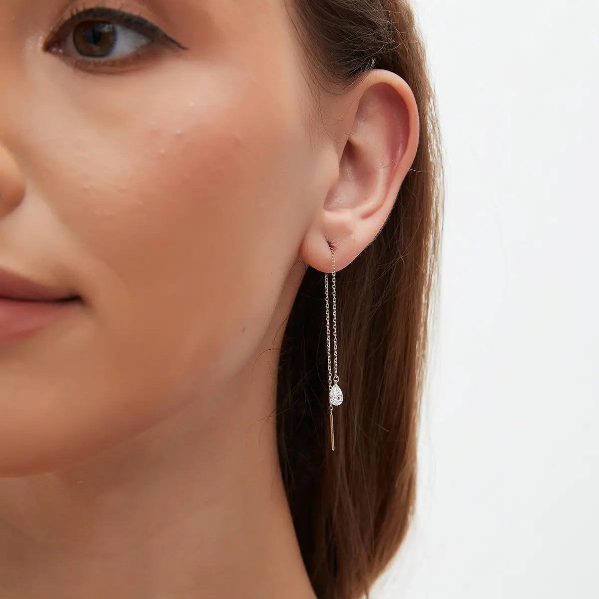 A curated ear stack demonstration showing the 18K gold pear diamond threader woven through two lobe piercings for a draped, layered effect. This styling shot illustrates the versatility of threader earrings in creating unique, personalized jewelry looks. The long gold chain adds verticality and motion, making it an ideal choice for pairing with gold studs and huggies. The image captures how the diamond catches the light from different angles during daily wear.