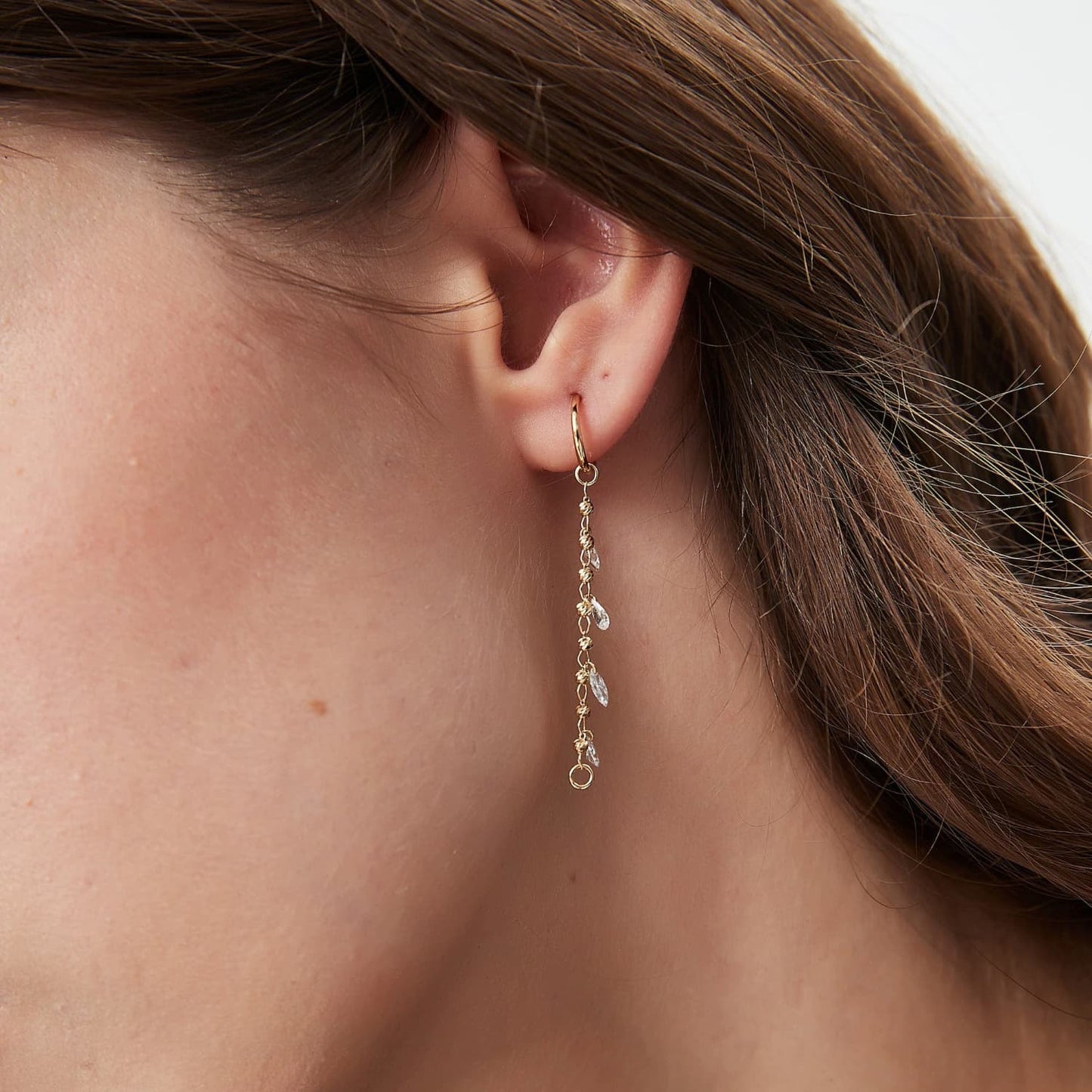 A lifestyle photograph showing the 18K gold charm linking two lobe piercings for a dramatic draped effect. Highlights the kinetic movement and versatility of the Celestial Drift design.