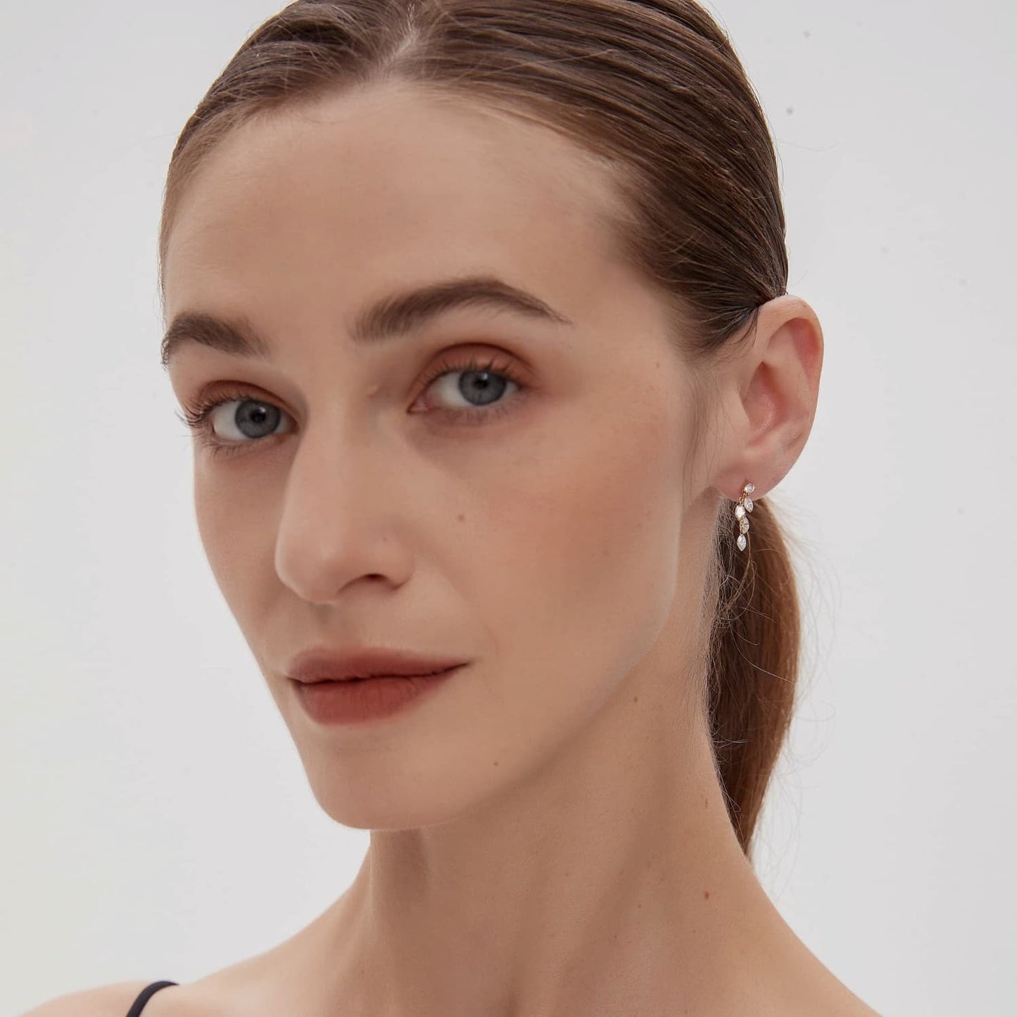 A fashion editorial photograph featuring the Round & Marquise Dangle Stud by LTM Jewels. The model is seen wearing the piece, illustrating its role as a cinematic heirloom and a bold statement of structural fluidity. The cascading diamonds sparkle brilliantly, complementing a high-end fashion aesthetic inspired by Vogue editorials. This image captures the atmospheric grace of the piece, showing how it adds a dynamic, shimmering glow to a high-fashion look and luxury jewelry collection.