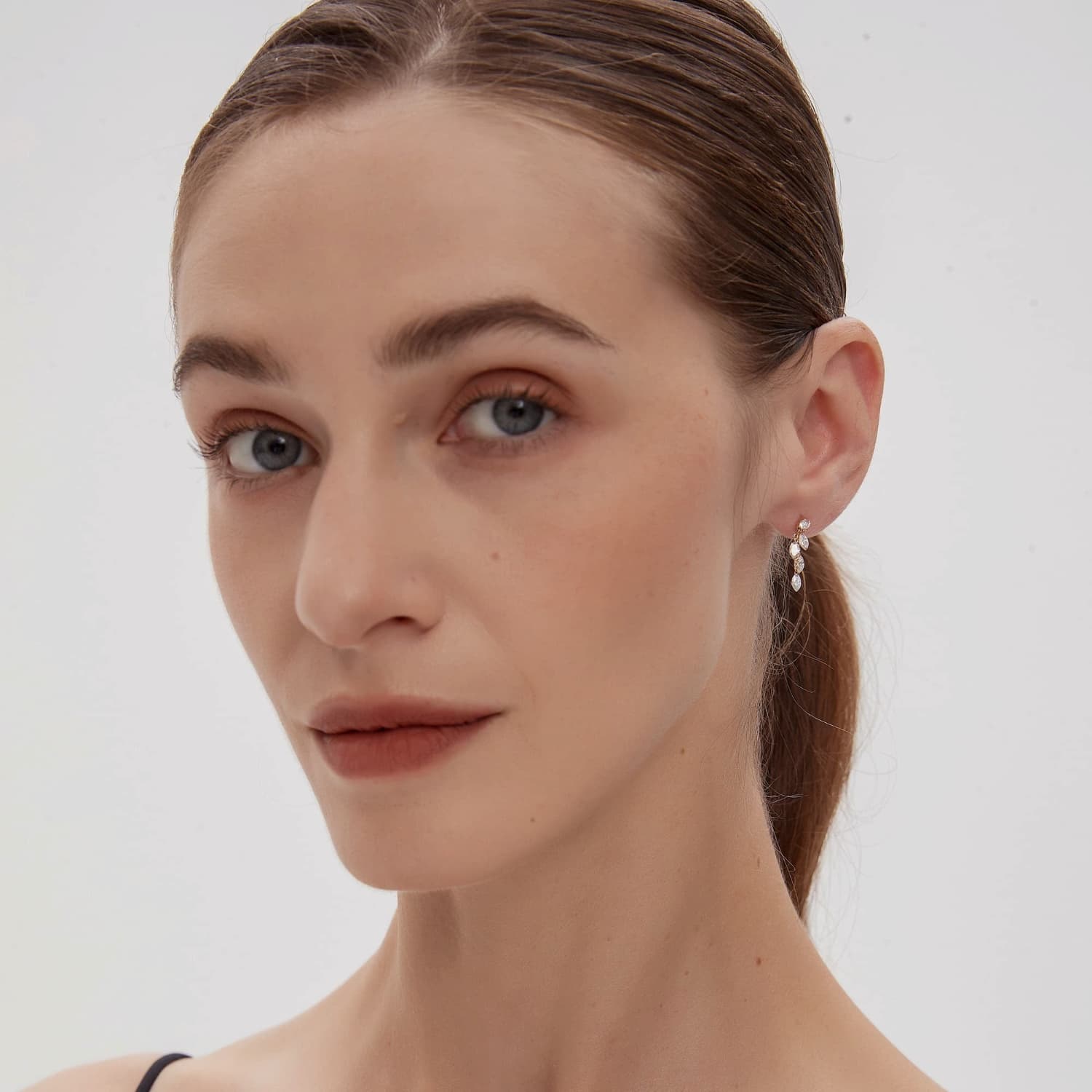 A fashion editorial photograph featuring the Round & Marquise Dangle Stud by LTM Jewels. The model is seen wearing the piece, illustrating its role as a cinematic heirloom and a bold statement of structural fluidity. The cascading diamonds sparkle brilliantly, complementing a high-end fashion aesthetic inspired by Vogue editorials. This image captures the atmospheric grace of the piece, showing how it adds a dynamic, shimmering glow to a high-fashion look and luxury jewelry collection.