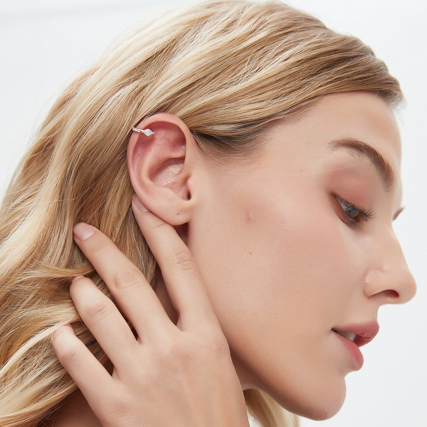 A professional lifestyle photograph showing the Lozenge Pavé Hoop styled on a model's ear. The 9mm 18K solid gold hoop demonstrates its architectural precision and edgy grace within a curated ear stack. This perspective highlights the unique geometric lines and how the pavé diamonds capture light from multiple angles for a cinematic radiance. Captured in natural lighting to emphasize the fire of the D-E color stones, illustrating a modern high-fashion approach to luxury jewelry styling.hoops