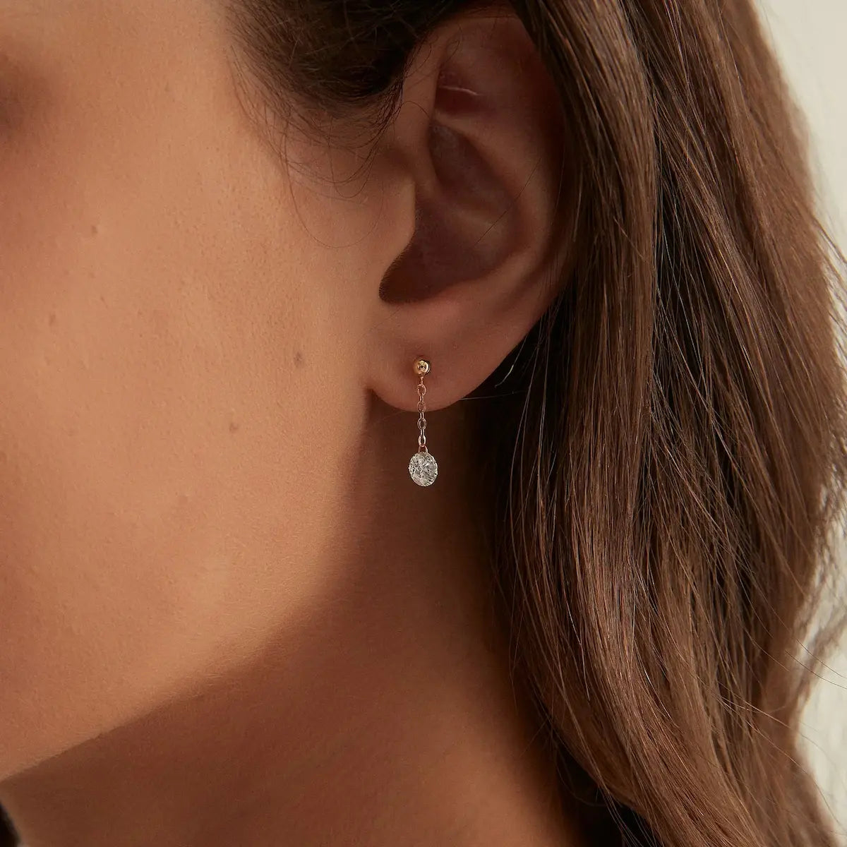 Macro close-up of the Round Chain Dangle Threaded Stud handcrafted in solid 18K gold. The suspended floating round diamond and delicate gold chain create uninterrupted brilliance, fluid movement, and refined architectural craftsmanship inspired by contemporary fine jewelry design.