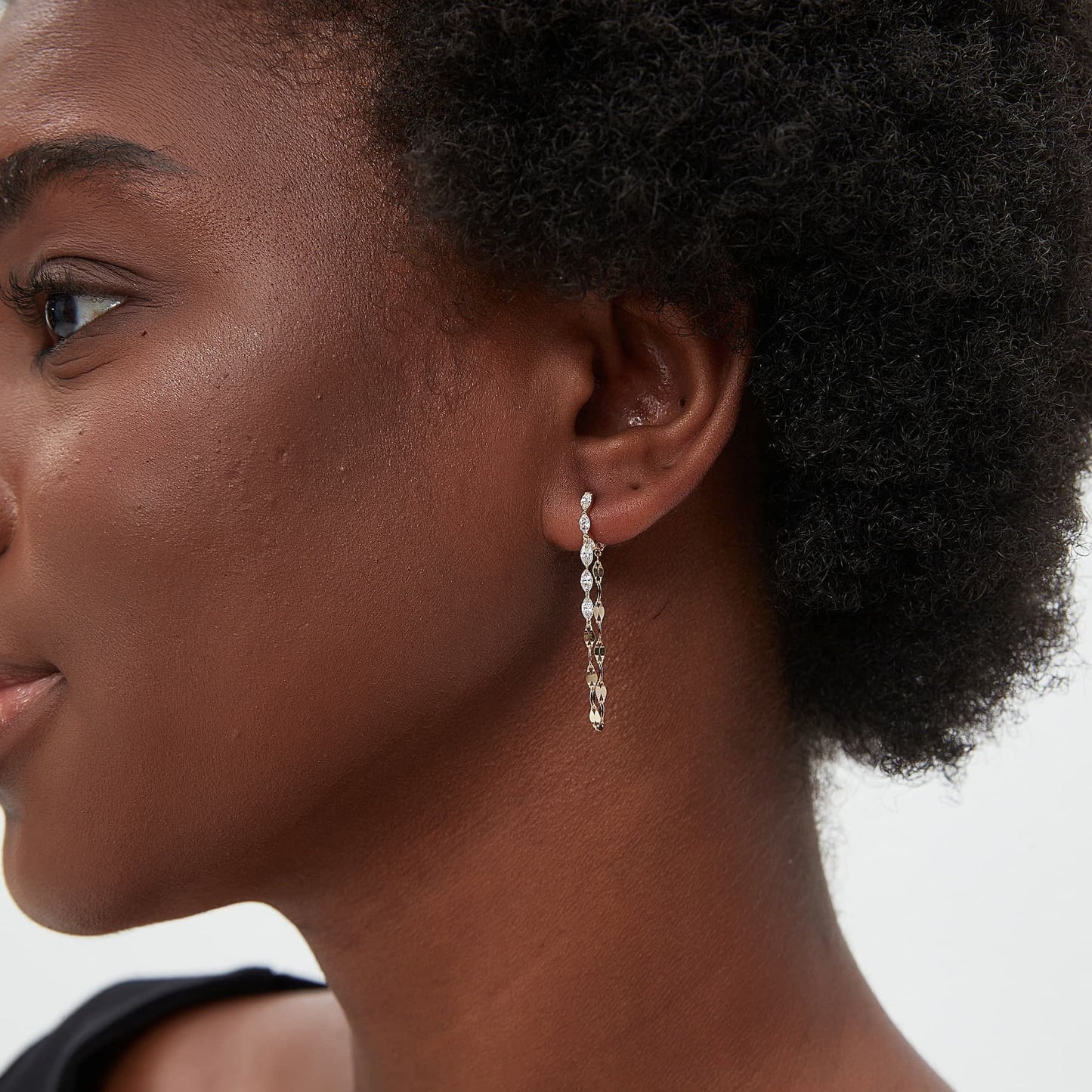 A lifestyle model shot of a woman wearing the Geometric Sway collection Marquise and Chain Dangle White Diamond Hoop in 18K solid gold. The photograph captures the natural brilliance of the eight white lab diamonds and the elegant movement of the dangling chain as it catches the light. This luxury jewelry piece by LTM Jewels embodies modern elegance and structural beauty, making it an ideal gift for an anniversary or a unique addition to a woman’s sophisticated fashion jewelry collection.