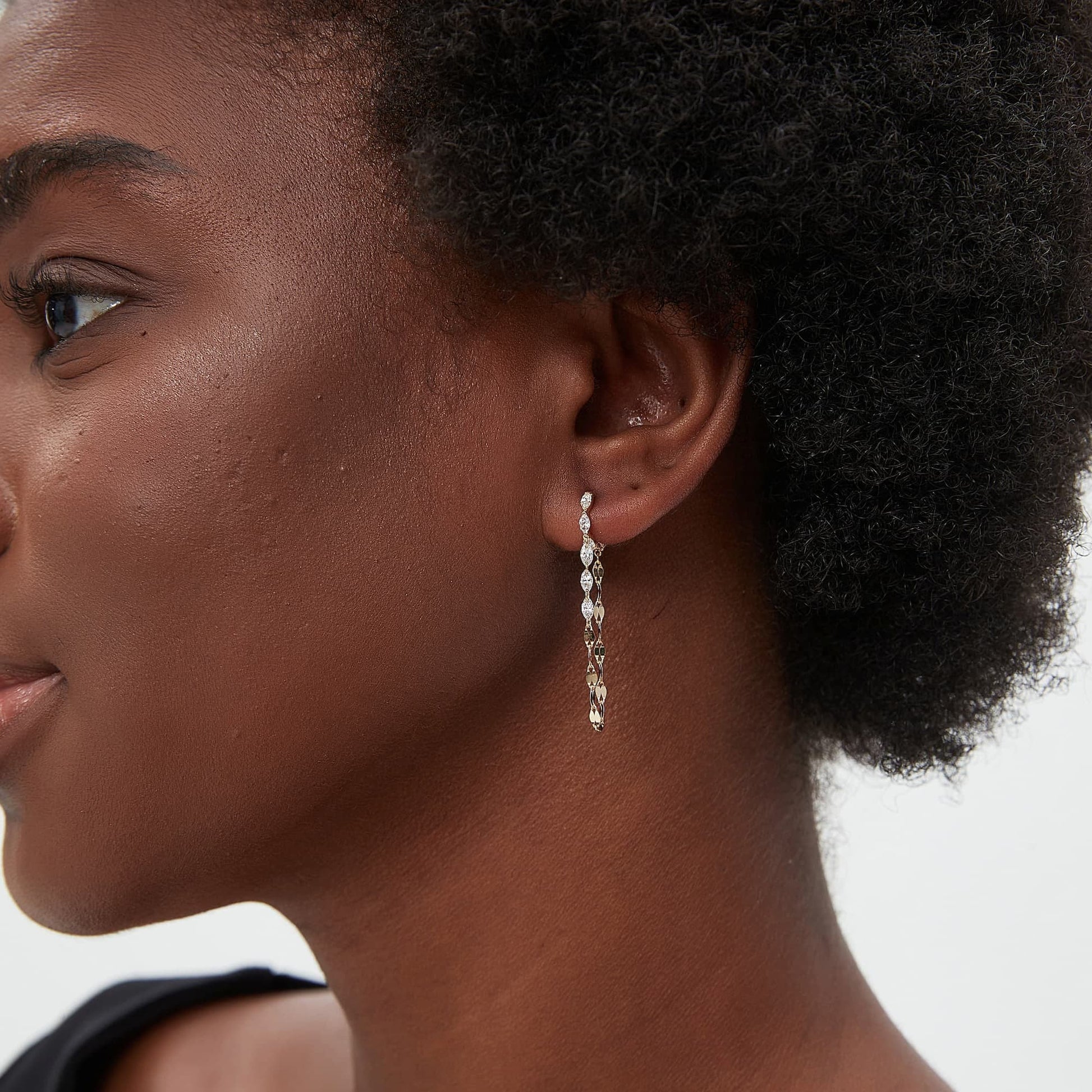 A lifestyle model shot of a woman wearing the Geometric Sway collection Marquise and Chain Dangle White Diamond Hoop in 18K solid gold. The photograph captures the natural brilliance of the eight white lab diamonds and the elegant movement of the dangling chain as it catches the light. This luxury jewelry piece by LTM Jewels embodies modern elegance and structural beauty, making it an ideal gift for an anniversary or a unique addition to a woman’s sophisticated fashion jewelry collection.