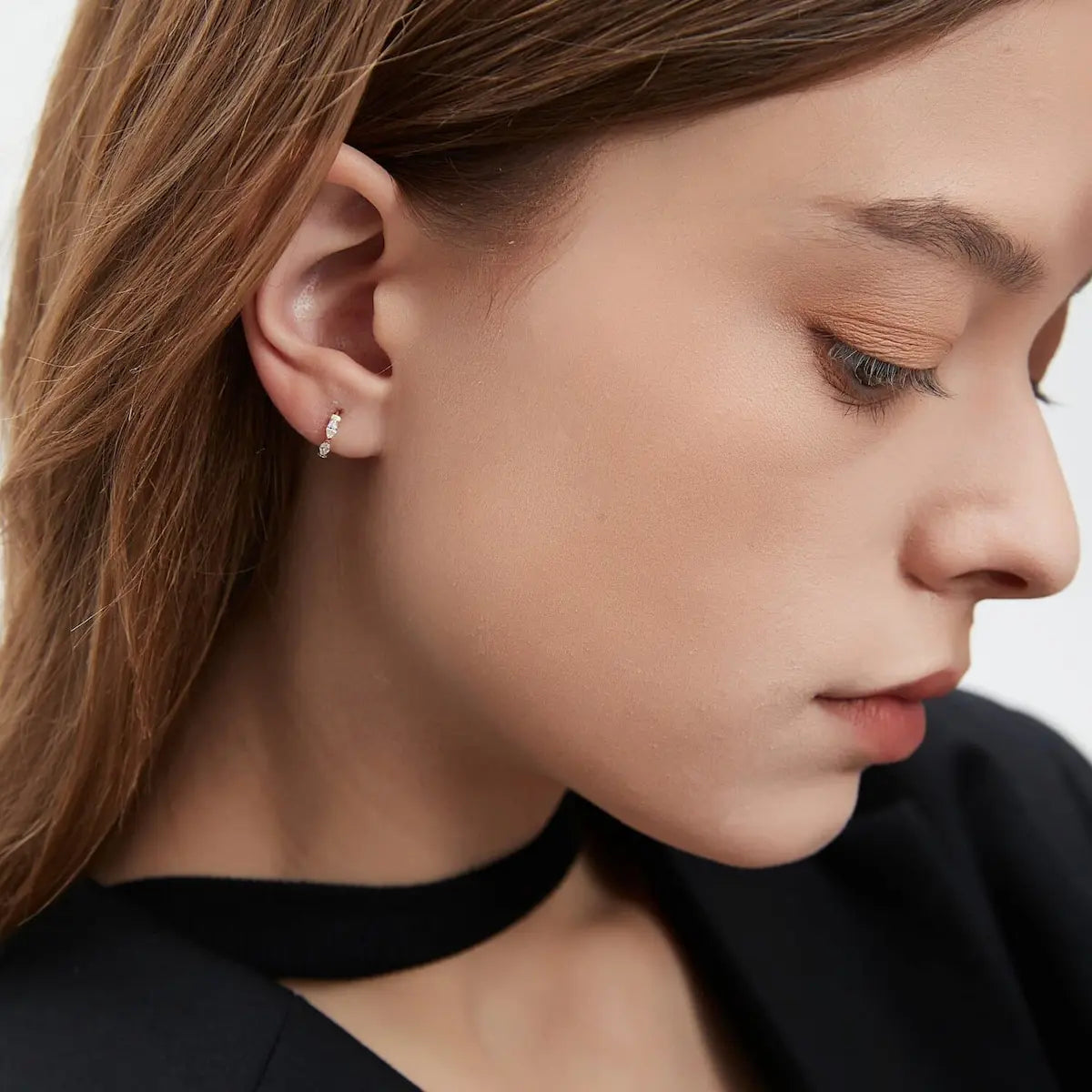 A sophisticated curated ear stack featuring the Marquise Row Diamond Hoop in a lobe piercing. The styling shot illustrates how the marquise silhouette adds elongated elegance and a continuous sparkle compared to round stones. Perfectly paired with 18K gold studs, this image demonstrates the hoop's versatile fit for lobe or helix placements, highlighting its comfortable 24/7 wearability and its ability to capture light during natural movement.