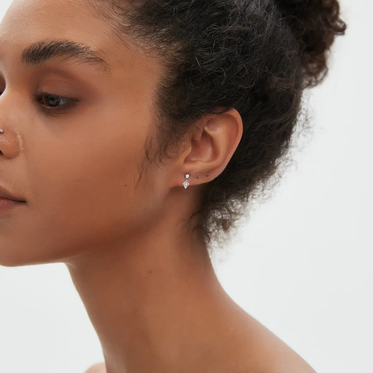 Lozenge Dangle Threaded Stud worn on the ear featuring a floating lozenge-cut diamond and suspended round diamond accent crafted in solid 18K gold. The lightweight geometric silhouette creates elegant movement and contemporary curated ear styling with architectural luxury