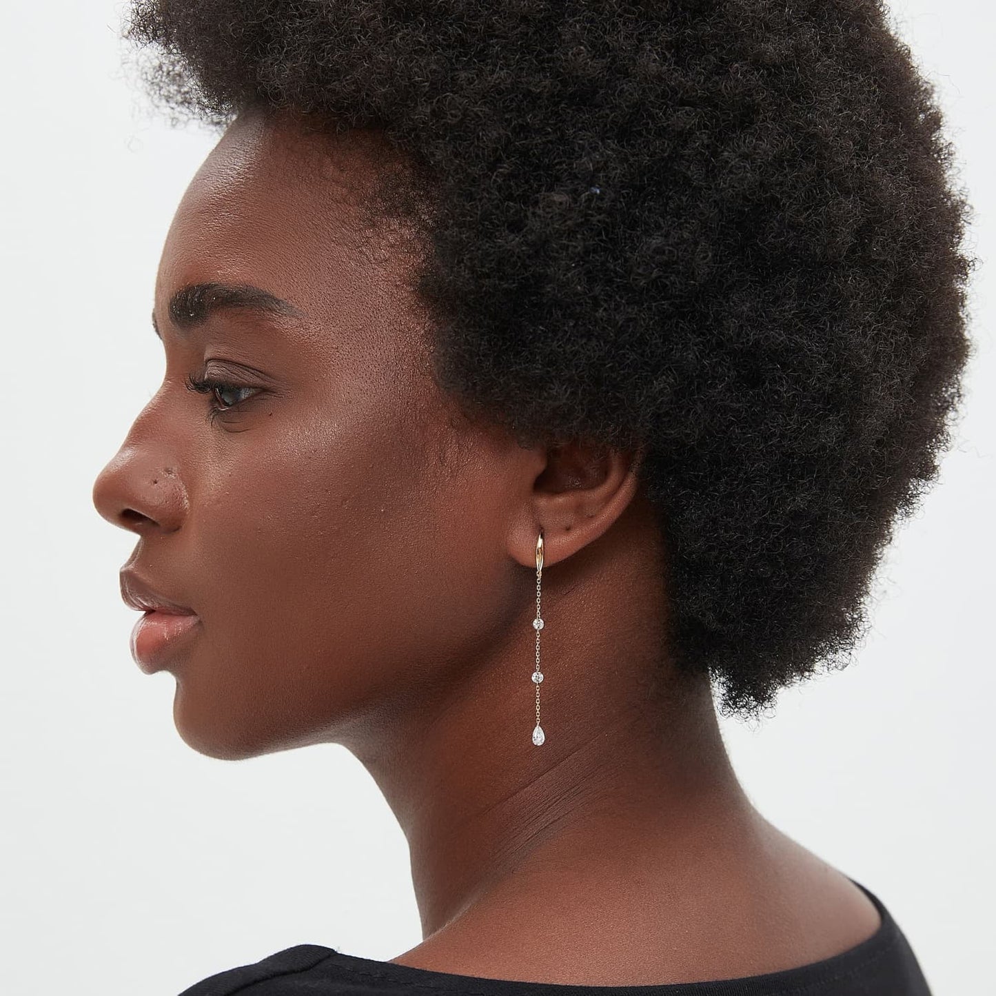 A lifestyle photograph of the Radiant Drift chain hoop worn on an ear. Highlights the elongated silhouette and how the diamond sequence captures light with movement within a high-fashion, curated ear stack.