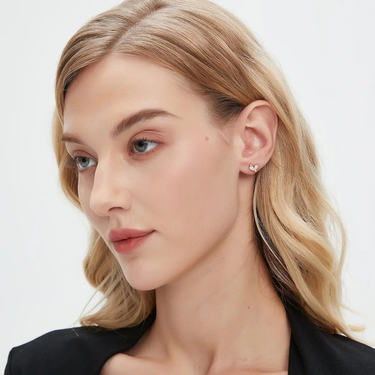 A professional lifestyle photograph showing the Eternal Heart Pear Diamond Stud styled on a model's ear. The image demonstrates how the two pear-cut diamonds create a radiant heart silhouette within a curated ear stack. This perspective highlights the minimalist staple design and the intense sparkle of the 0.40ctw diamonds in a real-world setting. Captured in natural lighting to emphasize the crystalline fire of the D-E color stones, perfect for modern and gender-neutral jewelry inspiration.