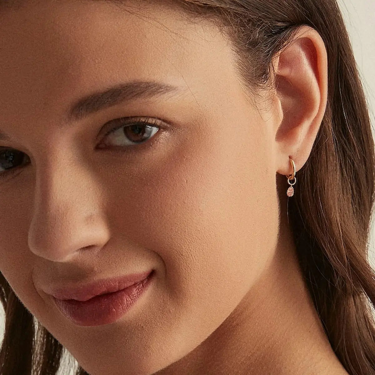 A professional lifestyle photograph showing the Blush Symphony Pink Pear Charm styled on an 18K solid gold hoop. The image demonstrates how the drill-set diamond captures light from every angle, adding a soft, cinematic glow to a curated ear stack. This perspective highlights the modularity and rhythmic movement of the charm in a real-world setting. Captured in natural lighting to emphasize the delicate fancy pink hue and the exceptional fire of the lab-grown diamond.