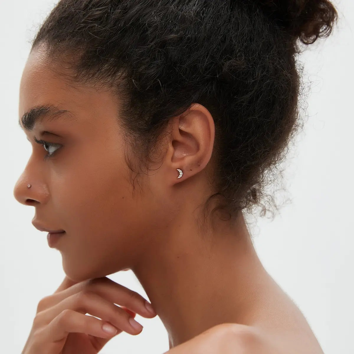 Diamond Crescent Moon Stud worn on the ear featuring natural white diamonds set within a curved crescent moon silhouette crafted in solid 18K gold. The lightweight sculptural structure creates celestial elegance and modern curated ear styling.