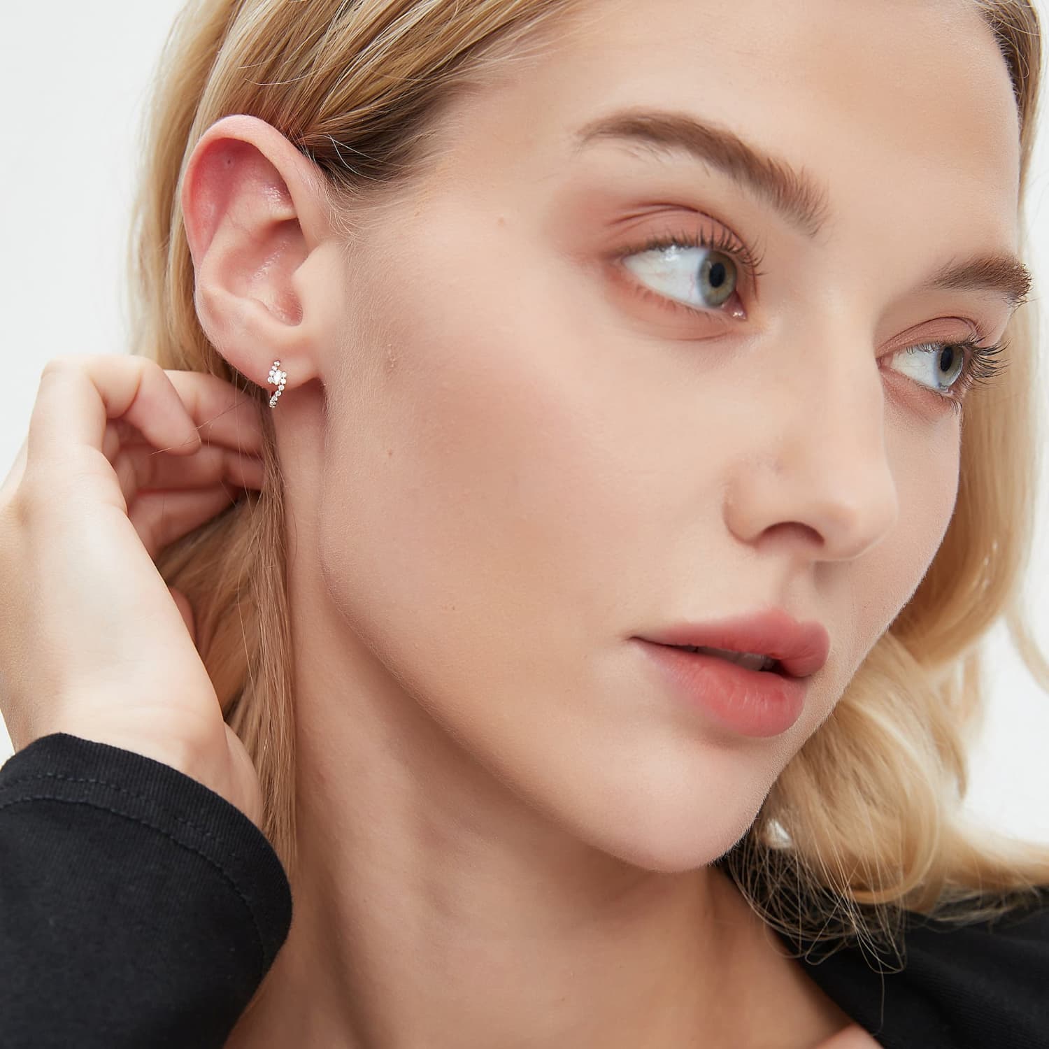 A professional lifestyle photograph showing the White Marquise Pavé Hoop styled on a model's ear. The 8mm 18K solid gold hoop demonstrates its rhythmic silhouette and effortless sparkle within a curated ear stack. This perspective highlights how the marquise diamonds wrap the ear, creating a structural and cinematic radiance. Captured in natural lighting to emphasize the crystalline fire of the D-E color stones.