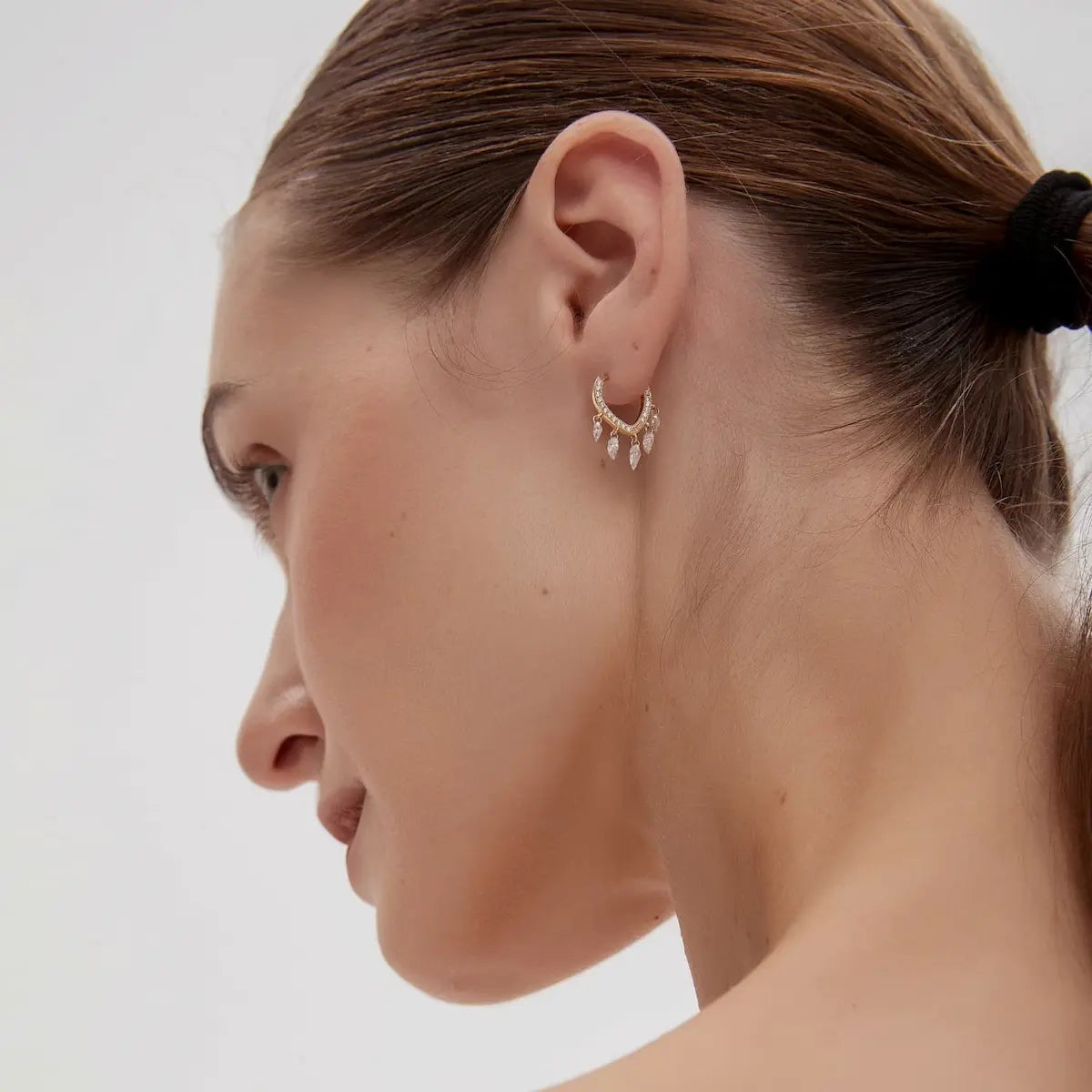 Lifestyle photography of a model wearing the LTM Jewels Eternal Radiance heart dangle hoop, showcasing its elegant motion and luminous glow in natural sunlight. The aesthetic emphasizes "refined luxury" and "romantic balance," proving the piece's suitability for sophisticated gifting or bridal jewelry. This shot demonstrates the earring's comfortable fit and hypoallergenic 18K solid gold construction, highlighting it as a durable, shower-safe investment for a modern jewelry collection.