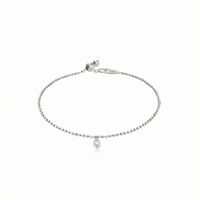 A high-resolution photo of the Pear Drilled Diamond Bracelet by LTM & CO.™. Features a 0.2ct laser-drilled pear diamond floating on an 18K solid gold diamond-cut bead chain. The image highlights the crystalline D-E color and VVS-VS clarity of the gemstone, showcasing the "Pure Brilliance" of the minimal setting which allows the diamond to catch light from every angle for a cinematic glow.