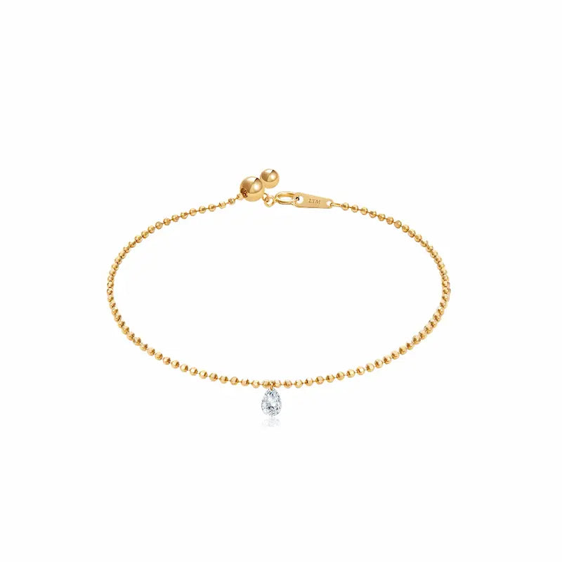 A high-resolution photo of the Pear Drilled Diamond Bracelet by LTM & CO.™. Features a 0.2ct laser-drilled pear diamond floating on an 18K solid gold diamond-cut bead chain. The image highlights the crystalline D-E color and VVS-VS clarity of the gemstone, showcasing the "Pure Brilliance" of the minimal setting which allows the diamond to catch light from every angle for a cinematic glow.