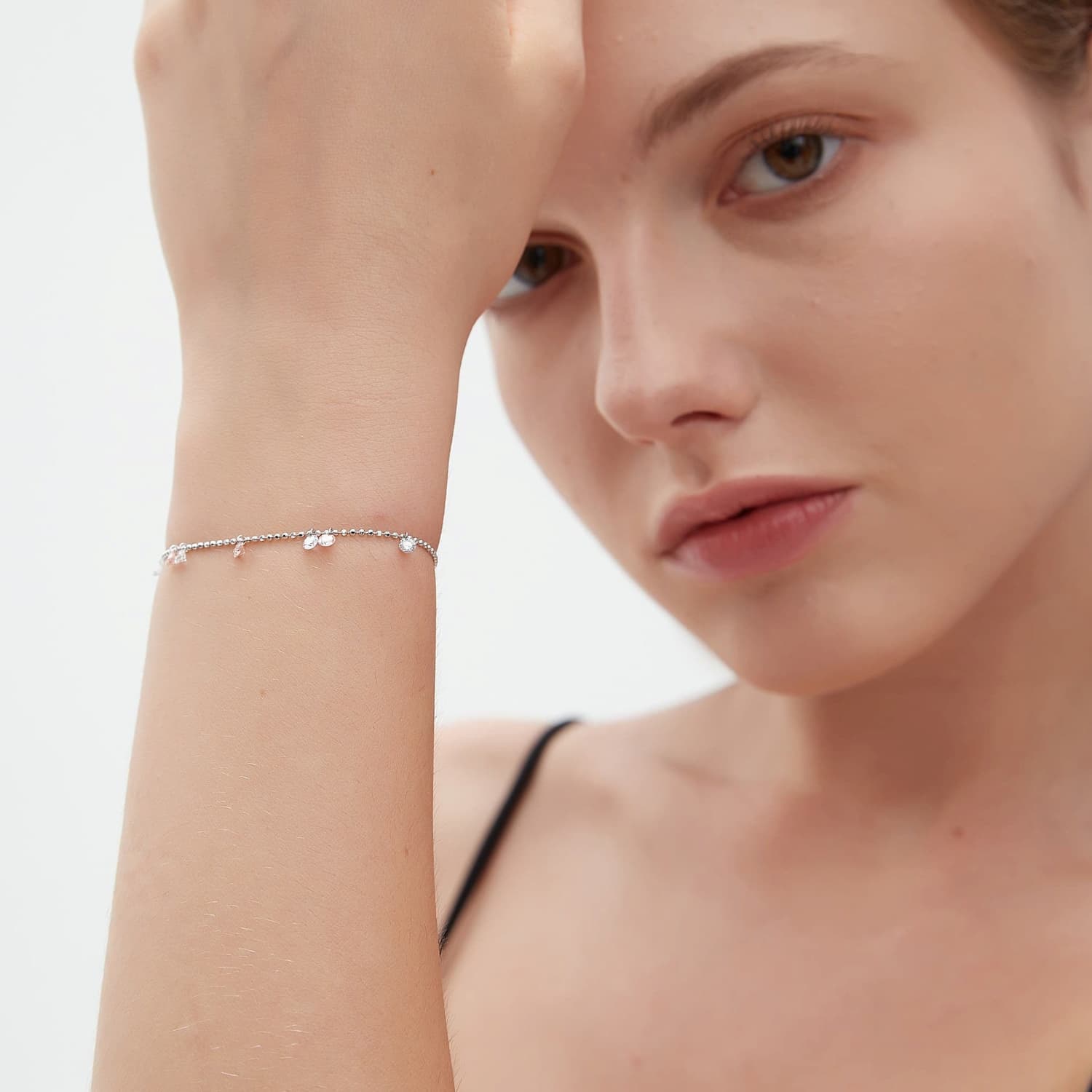 A lifestyle shot featuring the LTM Jewels Pink White Diamond Bracelet styled on a model's wrist. The image demonstrates how the laser-drilled diamonds catch the light during natural movement, creating a luminous glow against the skin. The shimmering 18K solid gold bead chain adds a sophisticated texture to the curated wrist stack. This perspective highlights the bracelet's fluid silhouette and delicate proportions, showcasing its romantic and ethereal quality in a real-world setting.