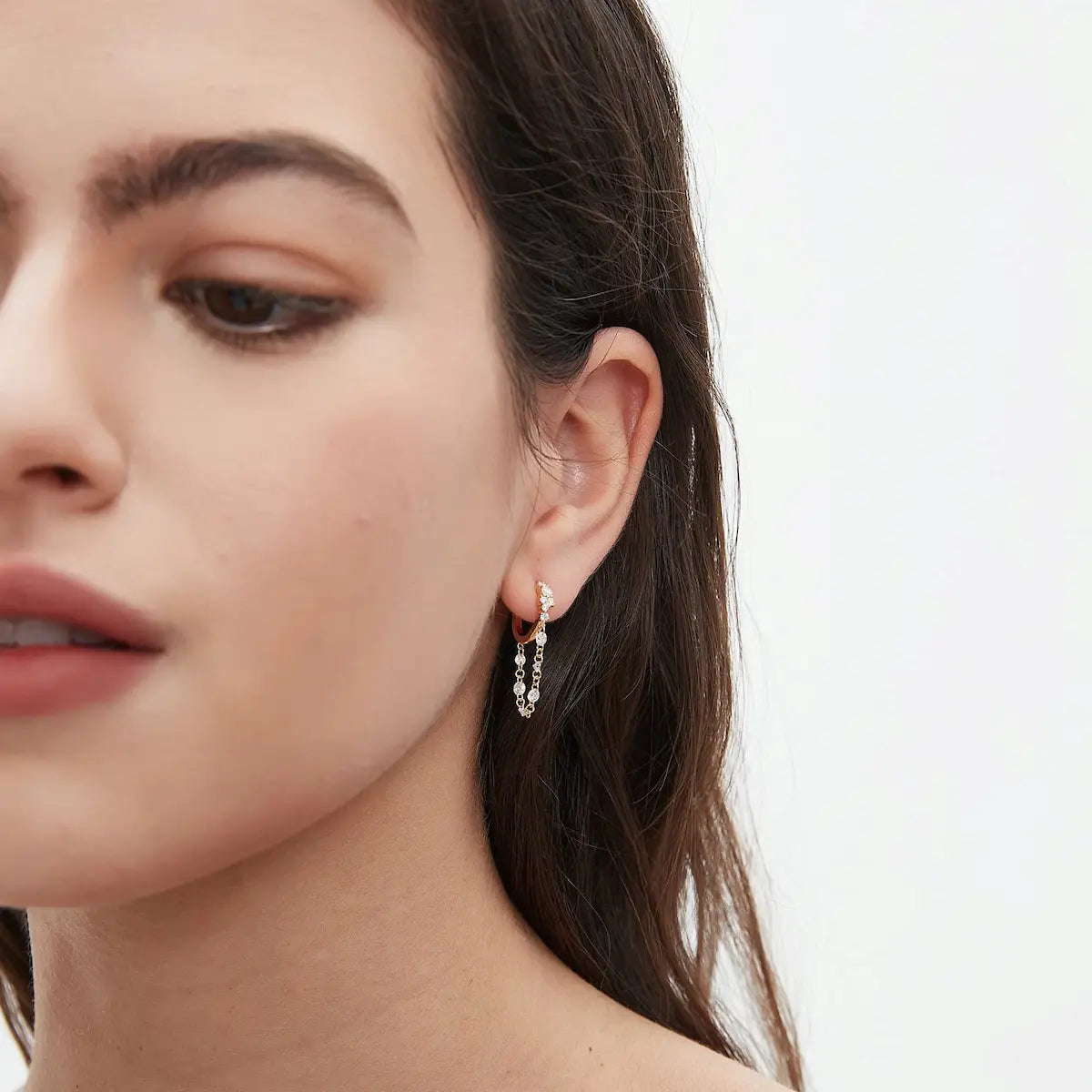 Professional ear stack curation featuring the Radiant Cascade diamond dangle hoop in a lobe piercing. The shot illustrates the vertical movement and shimmering waterfall effect of the floating diamond chain against the skin. Perfectly paired with other 18K gold studs and huggies, this image demonstrates the piece's ability to add high-fashion volume and rhythmic light to a sophisticated jewelry look, emphasizing its comfortable 8mm fit for daily luxury and 24/7 permanent wear.
