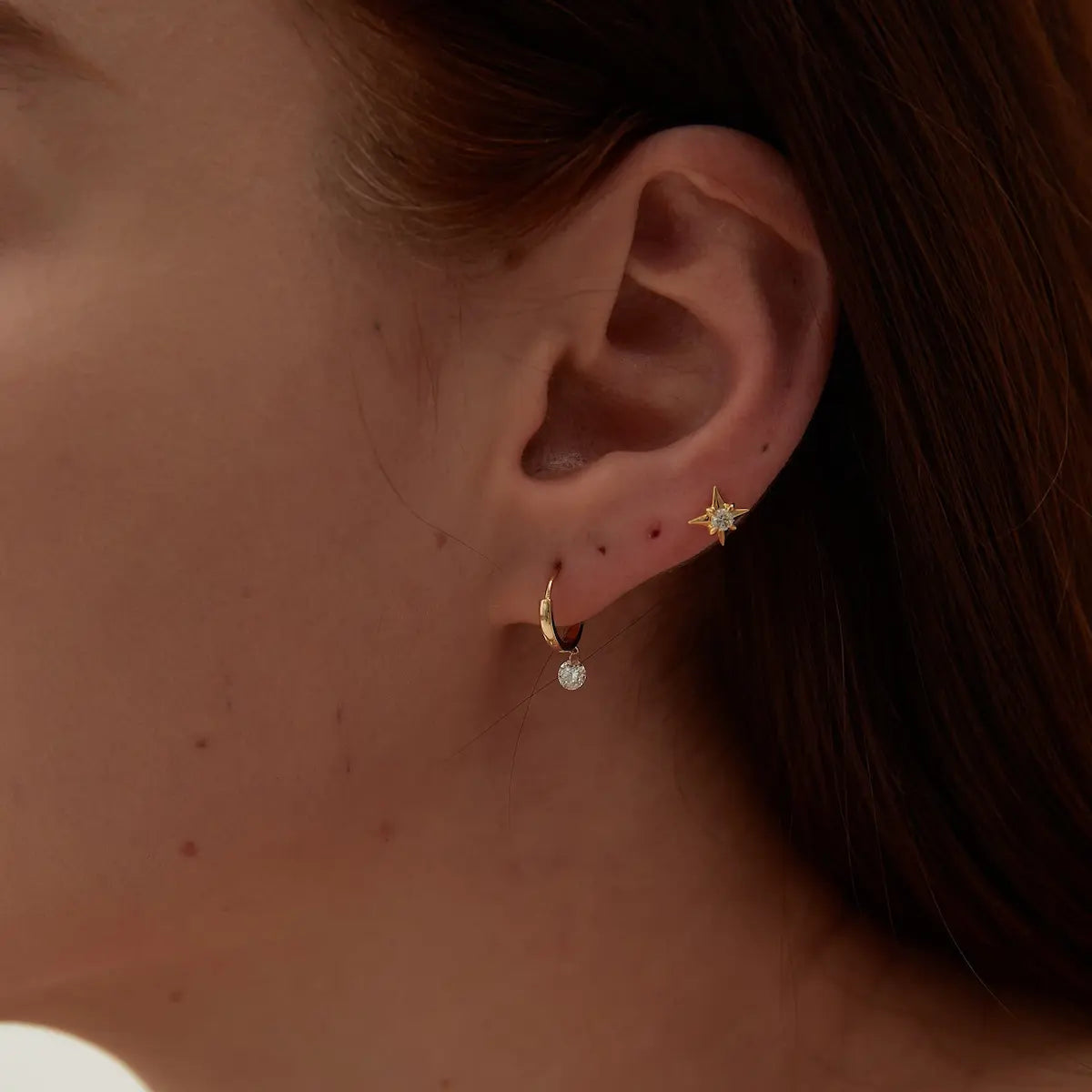 Macro close-up of the Round Diamond Dangle Hoop handcrafted in solid 18K gold. The suspended floating round diamond and polished hoop structure create uninterrupted brilliance, fluid movement, and refined architectural craftsmanship inspired by modern fine jewelry design.