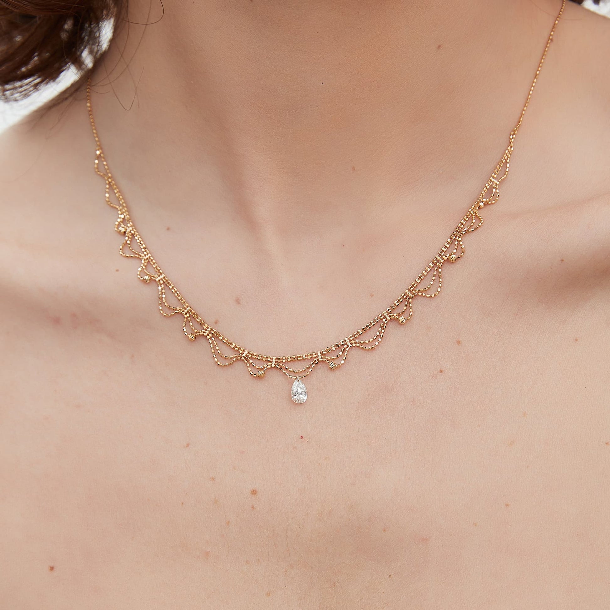 Detail of the 18K gold scalloped lace and signature 0.4ct pear diamond.