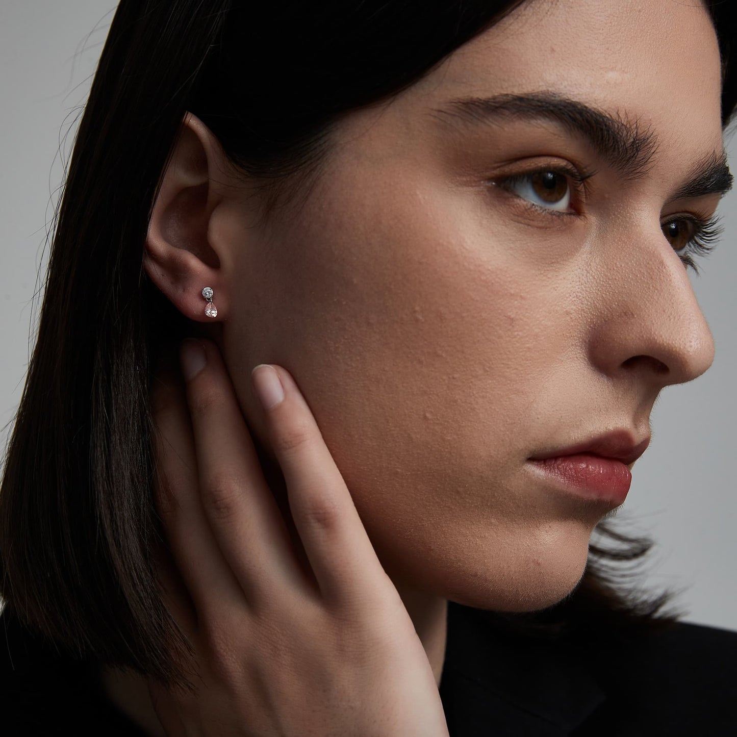 A fashion editorial photograph featuring the Pink Pear White Round Stud by LTM Jewels. The model is seen wearing the stud, illustrating its role as a cinematic heirloom and a sophisticated statement piece. The contrast between the romantic pink pear and the brilliant white round diamond is prominent, illustrating the Radiant Drift design philosophy. This image captures the atmospheric grace of the piece, showing how it adds a modern, structural glow to a high-end fashion look and luxury jewelry collection.