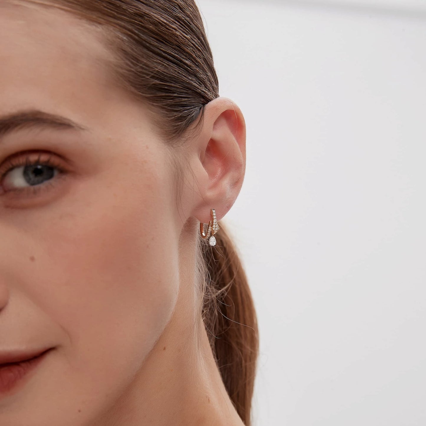Professional ear styling photography featuring the Serpentine Snake White Diamond Pear Drop Hoop in 18K gold, worn in a primary lobe piercing. The earring's 10mm inner diameter provides a secure and elegant fit, while the dangling pear diamond creates a rhythmic sparkle within a curated modern ear stack. This visual guide demonstrates the hoop's versatility for helix or cartilage placements, illustrating a sophisticated, high-fashion glow for both daily wear and special occasions.