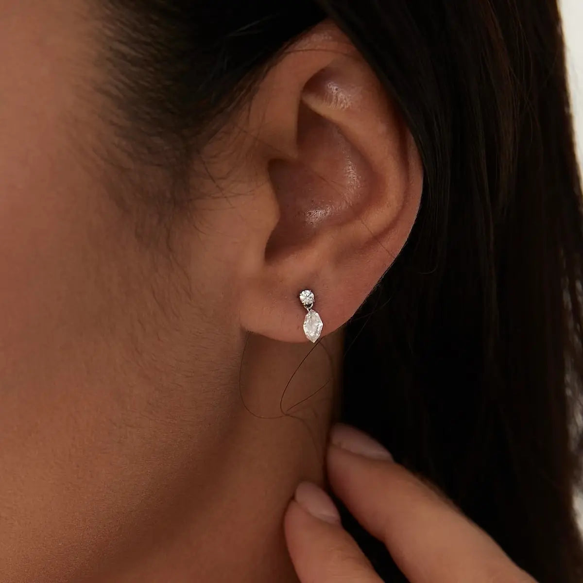A professional lifestyle photograph showing the LTM & CO.™ step-cut marquise dangle stud worn on a model's ear. The kinetic design sways gracefully, demonstrating its fluid movement and how it catches natural light. This perspective illustrates how the piece adds a sophisticated, structural glow to a curated ear stack, emphasizing the elongated silhouette and the high-polish finish of the 18K gold handcrafted setting.