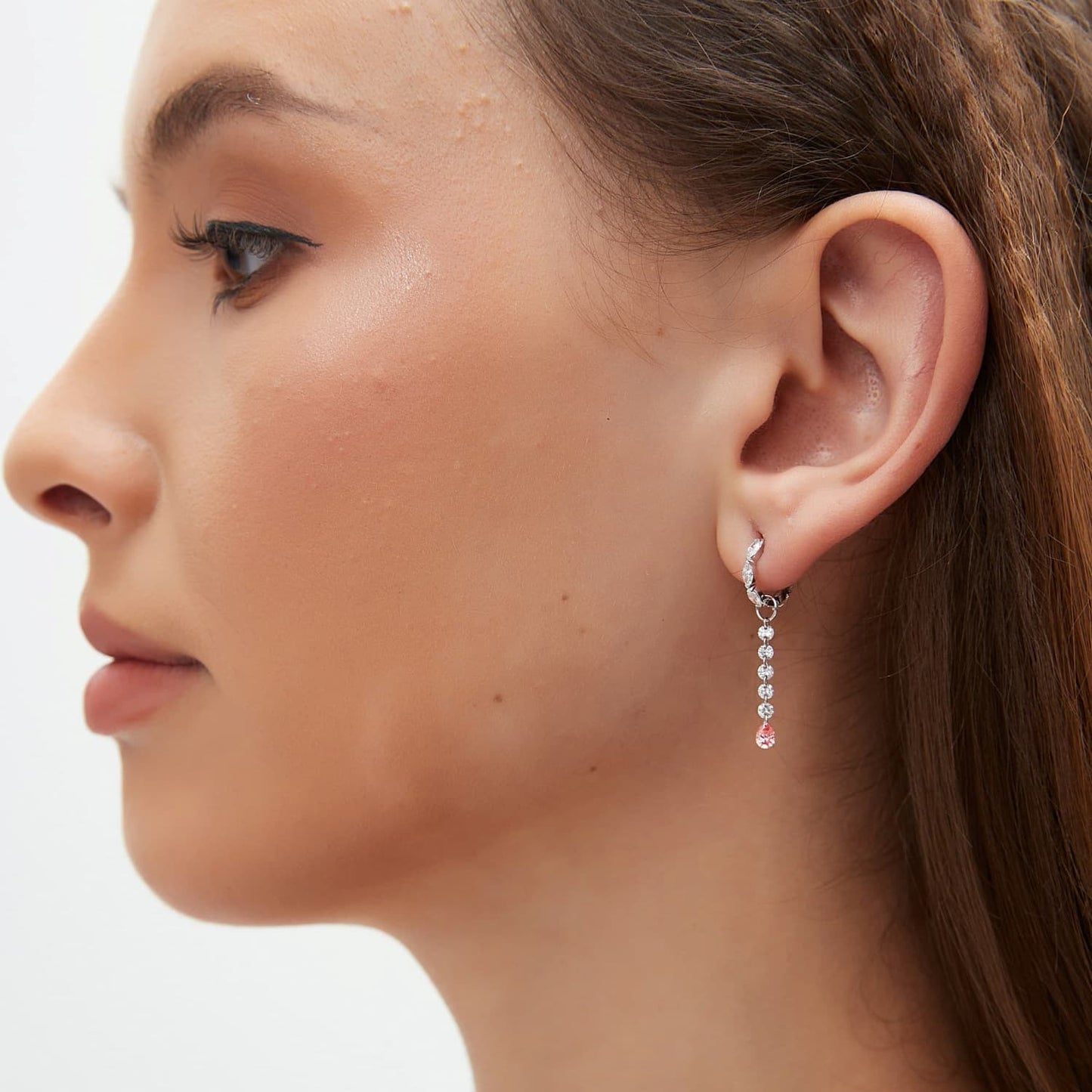 A professional lifestyle photograph showing the Blush Pink Pear Diamond Drop Charm styled on an 18K gold hoop. This image demonstrates the fluid motion and sophisticated movement of the floating pink pear as it catches the light. This perspective illustrates how the charm adds a rare color pop and cinematic radiance to a curated luxury ear stack, emphasizing the modular design for personalized and high-fashion everyday wear.