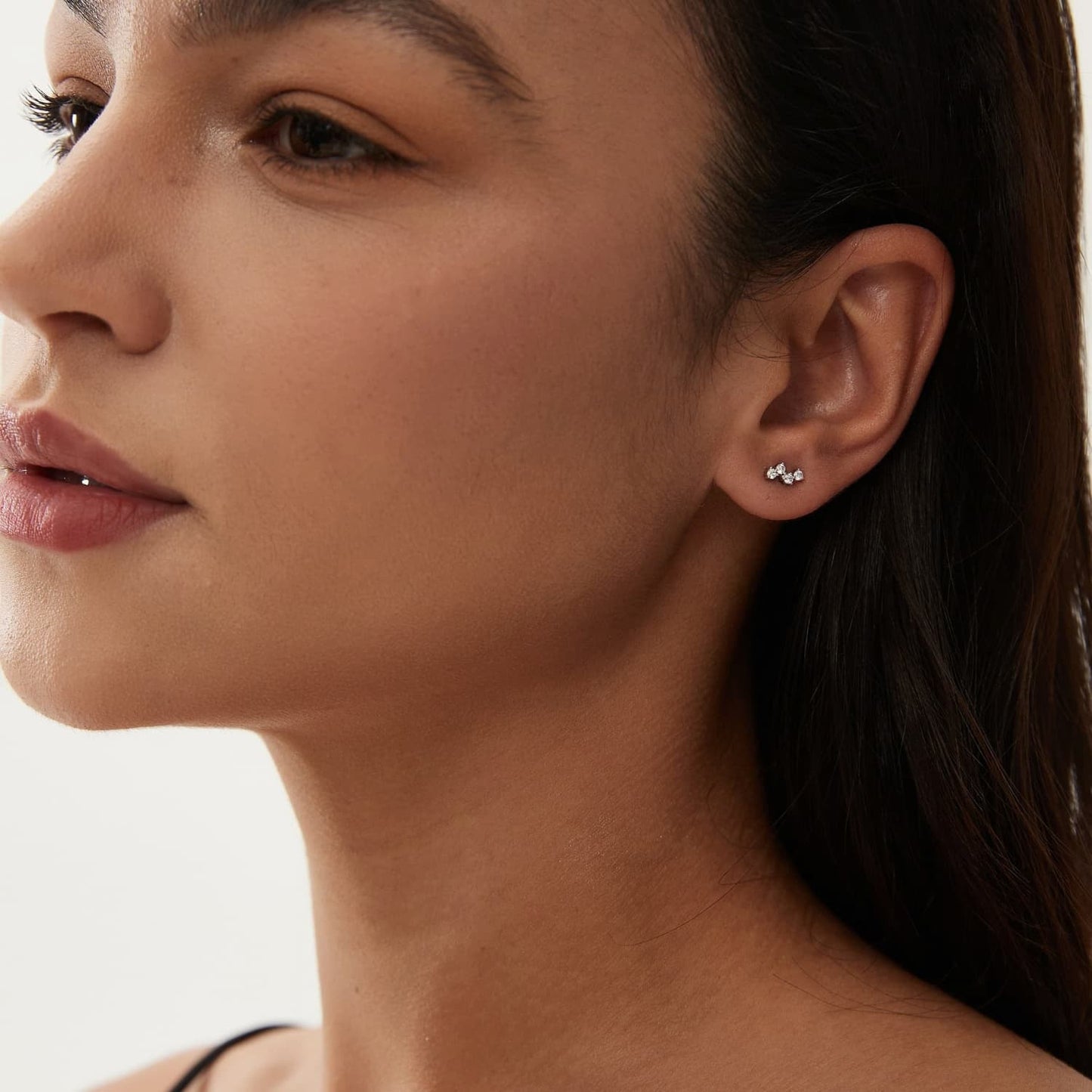 A lifestyle photograph showing the White Diamond Threaded Stud styled on a model's ear. The image demonstrates how the 18K solid gold setting and its brilliant white diamonds create a timeless clarity within a curated ear stack. This perspective highlights the versatile placement of the stud, showcasing its delicate and modern rhythm on the lobe or helix. Captured in natural lighting to emphasize the crystalline fire of the D-E color diamonds, perfect for luxury jewelry inspiration.