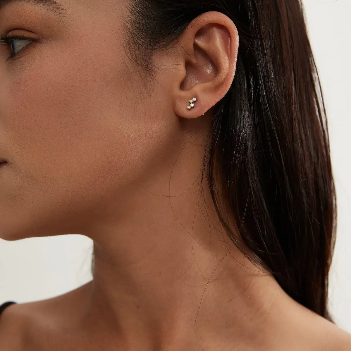 A professional lifestyle photograph showing the LTM & CO.™ Double Yellow White stud styled in a cartilage piercing. The minimalist heirloom design demonstrates its "Solar Radiance," reflecting a golden glow that catches natural light. This perspective illustrates how the small-scale brilliance adds a sophisticated, cinematic radiance to a curated luxury ear stack, emphasizing its suitability for permanent 24/7 wear and modern architectural aesthetics.
